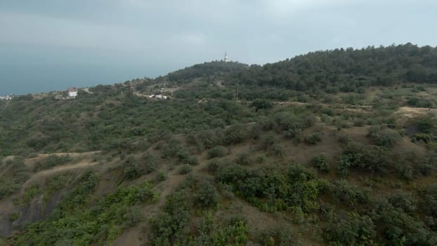 Top view of mountains with sea horizon and lighthouse. Shot. Beautiful landscape with mountains on coast and sea in distance.