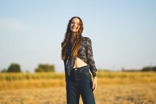 On a sunny day, a cheerful young woman with long hair finds joy in nature, posing in a golden field that radiates warmth and freedom, embodying a carefree spirit and relaxed lifestyle