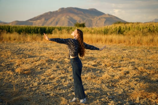 A carefree individual stands in the middle of a vast, open field, arms fully outstretched wide, delighting in the beauty and overwhelming tranquility of nature beneath a stunning mountain backdrop