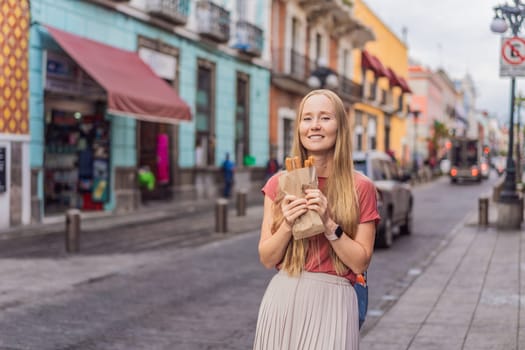 Female tourist eating churros on a colonial street in Puebla, Mexico. Cultural experience, local cuisine, and street food exploration concept.