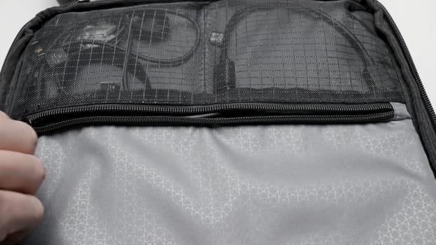 Close up of a male hand opens zipper lock of mesh pocket. Action. A backpack with charger wires
