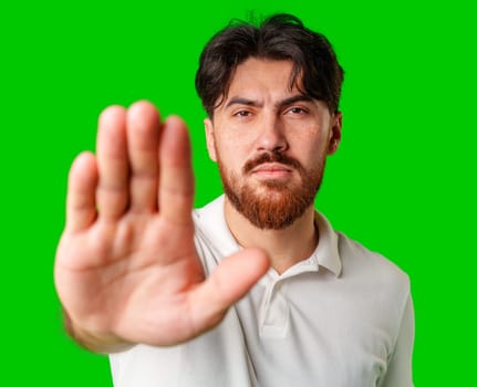 Man with a beard holding up his hand and looking at the camera against a bright green background in a neutral setting
