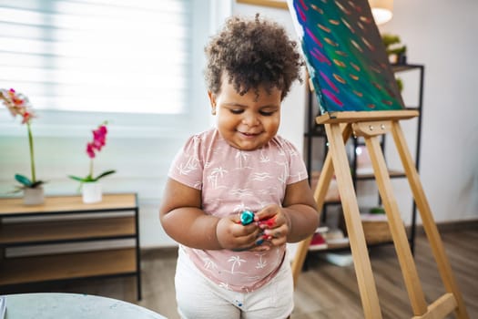 A young child happily creates art with colorful paints in their cozy home.