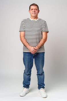A man stands confidently in a striped shirt, casual jeans with a neutral background in studio
