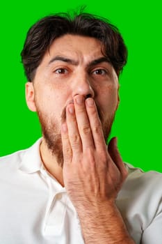 A man with a surprised expression holds his face while against a vibrant green background close up