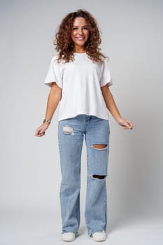 A woman in a white shirt and ripped jeans posing positively with a playful expression in a light studio setting close up