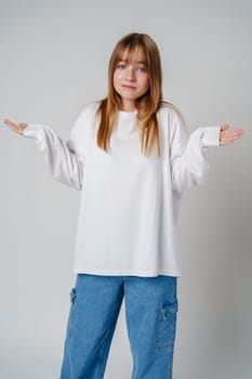 A young girl wearing a white long-sleeve shirt expressing confusion in a minimalistic gray studio setting close up