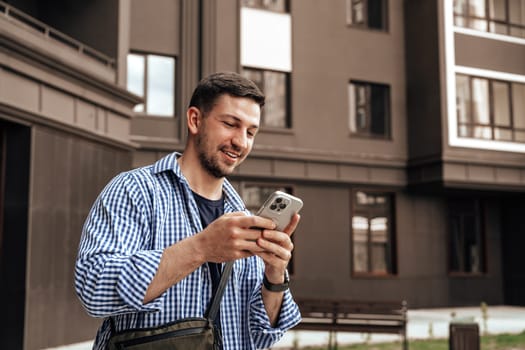 Young man happily using smartphone outside a modern building during daytime close up