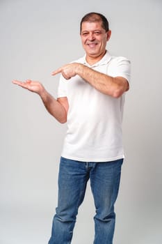 Man dressed in a white polo shirt and jeans happily pointing to the side against a plain background close up