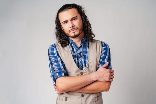A confident young man with curly hair poses against a neutral backdrop indoors