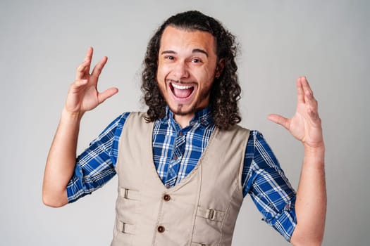 A man with curly hair excitedly gesturing while wearing a plaid shirt and vest against a plain background close up