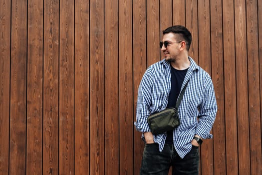 A man in a blue checkered shirt smiles while standing outside a modern building on a sunny day close up