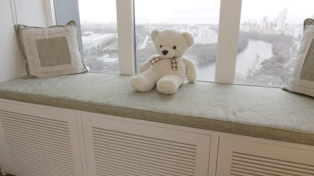 Teddy bear sits on a decorative windowsill. Creative. Cute white children toy bear near the window