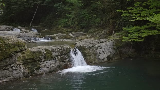 A small cascade and waterfall in lush green forest. Design. Natural background with a waterfall and green trees