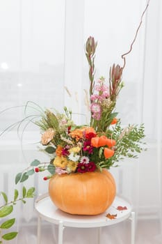 Flower arrangement in a pumpkin, autumn interior decor. Creating handmade autumn decor