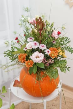 Flower arrangement in a pumpkin, autumn interior decor. Creating handmade autumn decor
