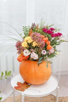 Flower arrangement in a pumpkin, autumn interior decor. Creating handmade autumn decor