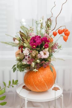 Flower arrangement in a pumpkin, autumn interior decor. Creating handmade autumn decor