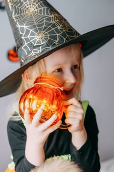Children's Halloween - a girl in a witch hat and a carnival costume with airy orange and black balloons at home. Ready to celebrate Halloween.