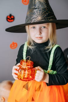 Children's Halloween - a girl in a witch hat and a carnival costume with airy orange and black balloons at home. Ready to celebrate Halloween.