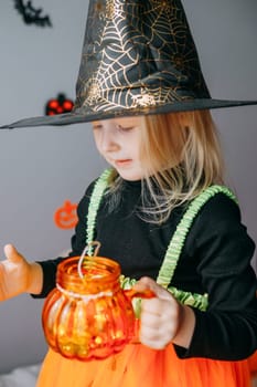 Children's Halloween - a girl in a witch hat and a carnival costume with airy orange and black balloons at home. Ready to celebrate Halloween.