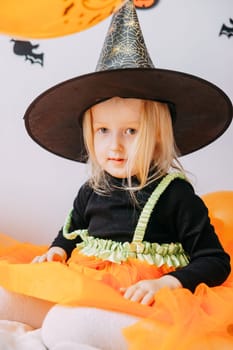 Children's Halloween - a girl in a witch hat and a carnival costume with airy orange and black balloons at home. Ready to celebrate Halloween.