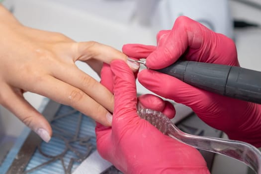 Nail technician carefully applies a nail drill for a detailed hardware manicure on a clients nails in the salon.