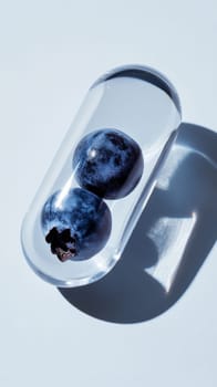 blueberries encapsulated in a clear capsule on blue background, modern health and wellness concept.