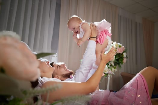 A couple enjoys a tender moment while their baby girl plays with a toy in a warm, inviting space filled with soft lighting on bed in beautiful room
