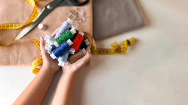 Colorful spools of thread in hands with sewing supplies on table.