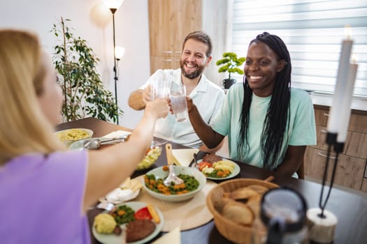 Three friends toast together while enjoying a delicious homemade meal.