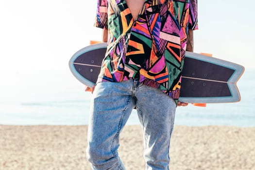 crop view of anonymous young hipster male skater in trendy summer outfit carrying skateboard while standing on embankment against sea and cloudless sky in summer