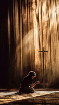 Young man kneels in prayer before a cross on a wooden floor, bathed in a dramatic light beam, evoking hope and spirituality