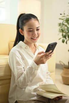 Beautiful young woman s sitting on floor at home and using mobile phone.