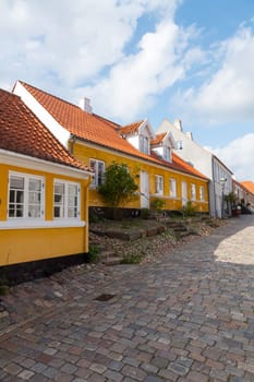 ebeltoft,denmark,30-08-2024:Quaint European street featuring vibrant buildings and cobblestone path under a blue sky. typical yellow houses