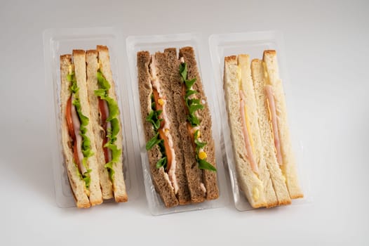 Three packaged sandwiches with white and whole wheat bread, filled with lettuce, tomatoes, turkey, cheese, ham and greens. Ideal for quick meals.
