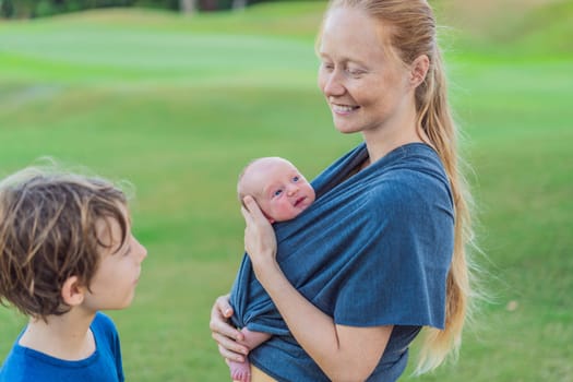 Mom walks with a newborn in a sling and also with her teenage son. This scene showcases the bond within the family, highlighting the nurturing care of a mother and the connection between siblings.