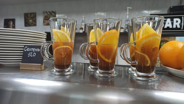 Glasses filled with aromatic tea and garnished with lemon slices are lined up on a counter, awaiting customers at a bustling cafe.