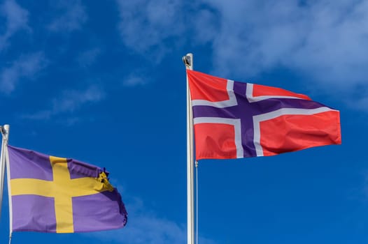 The vibrant flags of Sweden and Norway flutter proudly in the sunlight, reflecting their rich histories amidst a backdrop of clear blue skies, capturing a moment of unity and pride.