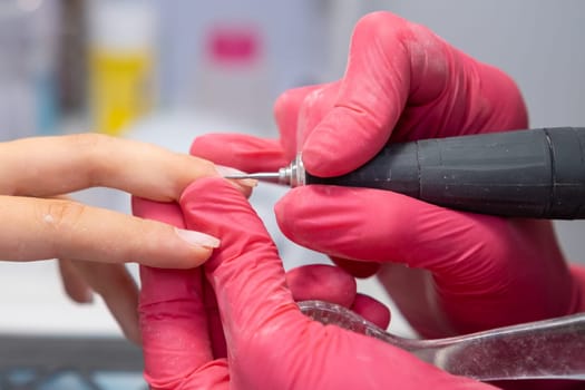 Manicurist uses a nail drill to perfect a woman hardware manicure in a beauty salon