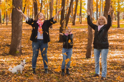 Grandmother and mother with granddaughter throw up fall leaves in autumn park and having fun. Generation, leisure and family concept