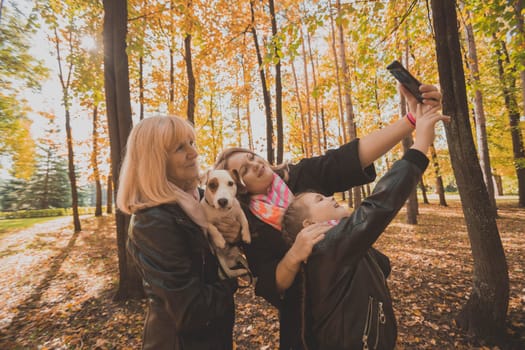 Three generations of women and dog feel fun look at camera posing for self-portrait picture together, funny excited child, mom and grandmother have fun enjoy weekend take selfie on gadget on autumn park