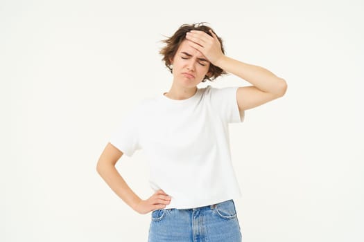 Health and people. Young woman has headache, touches her head and grimacing from painful migraine, feeling unwell, dizzy, standing over white background.