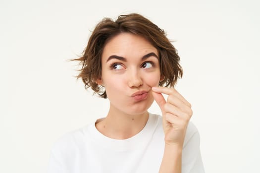 Image of young woman makes promise to keep secret, shows mouth zip gesture, puts a seal on her lips, dont talk sign, stands over white background.
