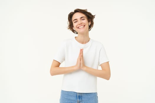 Portrait of brunette young woman holds hands together, namaste gesture, say thank you, grateful, express gratitude and joy, stands over white background. copy space