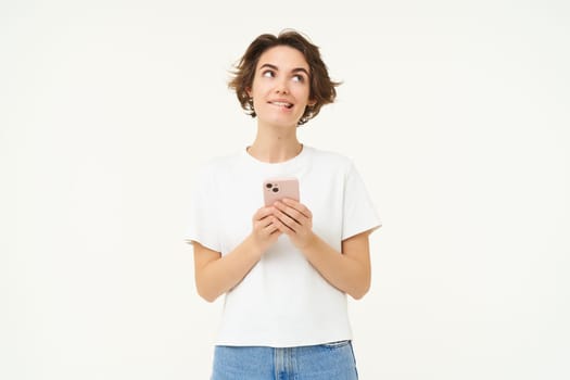 Portrait of brunette girl with smartphone, sending a message, using mobile phone application, smiling and looking happy, white studio background.