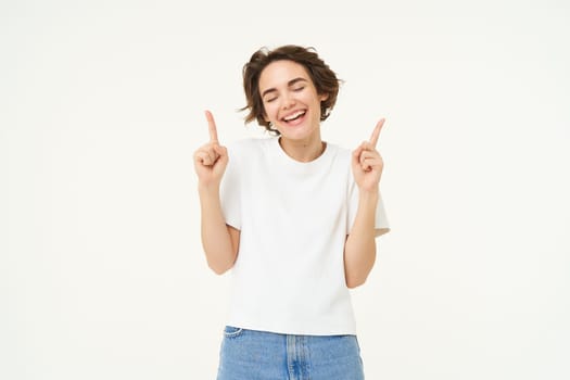 Image of carefree girl, laughing and smiling, pointing fingers up, showing promo offer, banner on top, posing over white studio background. Copy space