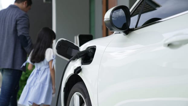 Progressive father and daughter installing plug from home charging station for electric vehicle. Future eco-friendly car with EV cars powered by renewable source of clean energy.