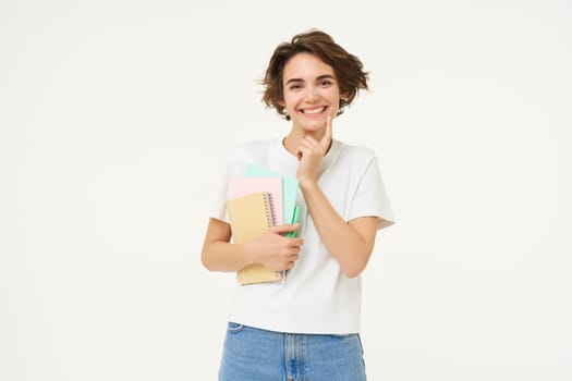 Image of stylish, modern girl student, holding workbook, documents. Woman teacher with papers standing over white background.