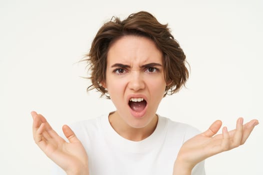 Close up of angru woman, looking shocked and frustrated, cant understand something, standing over white background. Copy space